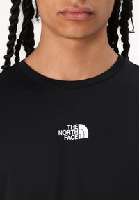 Camiseta de algodón negra con cuello redondo y mangas cortas. Presenta un logotipo blanco con el texto "THE NORTH FACE" y un elemento de diseño curvado.
