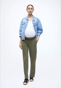 Φωτεινό γαλάζιο φαρδύ τζιν μπουφάν, λευκό αμάνικο τοπ, χακί παντελόνι με ελαστική μέση, μαύρα αθλητικά παπούτσια με λευκές και καφέ λεπτομέρειες.