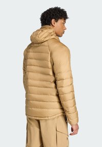 Jakna s kapuljačom u svijetlosmeđoj boji, s qulitiranim teksturom i elastičnom donjim rubom. Ima glatku, sjajnu površinu bez vidljivih metalnih dijelova.