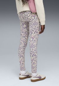 Leggings de couleur crème avec un motif abstrait ludique en violet et rose. La texture semble élastique ; la coupe est ajustée.