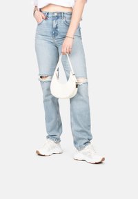 Jeans taille haute bleu clair avec des genoux déchirés, associés à un petit sac à bandoulière blanc et des baskets blanches, avec un tissu texturé.