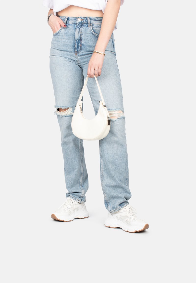 Jeans taille haute bleu clair avec des genoux déchirés, associés à un petit sac à bandoulière blanc et des baskets blanches, avec un tissu texturé.