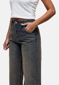 Jeans en denim à lavage foncé avec une taille haute, une coupe droite et un style classique à cinq poches. Comprend une fermeture à bouton en métal.