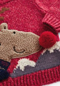 Pull en tricot rouge avec un devant en forme de visage d'animal en peluche brun affichant une expression souriante, un accent en pompon rouge et des motifs de montagne en violet clair et foncé.