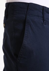 Pantalons en coton bleu marine avec une texture lisse et des détails cousus. Présente une petite étiquette logo sur la poche latérale.