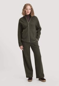 Giacca in pile verde oliva con zip frontale e tasche laterali, abbinata a pantaloni a vita alta coordinati. Tessuto testurizzato; vestibilità comoda.