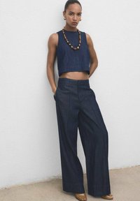 Un haut court en denim foncé et un pantalon large, avec une texture lisse. Accentué par un collier en perles de bois et un design minimaliste.