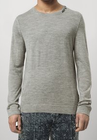 Hellgrauer langärmliger Strickpullover mit Rundhalsausschnitt und dezenten Steppdetails an den Schultern. Weiche Textur, schlanker Schnitt.