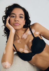 Melnas mežģīņu krūšturis ar ribotu audumu, mīkstām kausēm un regulējamām siksnām. Ievērojama viļņota mežģīņu apdare augšpusē. Gluda tekstūra.