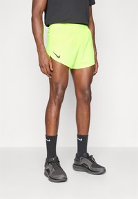 Shorts Nike giallo neon con logo nero, abbinati a calze nere e scarpe sportive grigio scuro. Tessuto liscio, design leggero.