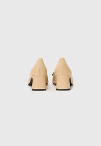 Chaussures à talons hauts en cuir beige avec un bout pointu et un talon carré. Texture lisse et design minimaliste, avec une semelle noire.