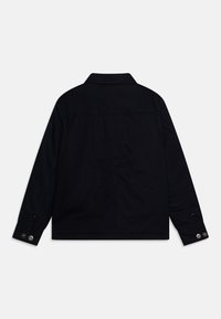 Schwarze Jeansjacke mit Kragen, langen Ärmeln und Knopfmanschetten; hat einen geraden Schnitt und minimale Details auf der Rückseite.