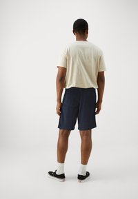 Marineblauwe shorts met een ontspannen pasvorm en een achterzak, gecombineerd met een lichtbeige t-shirt, aangevuld met zwarte sneakers en witte sokken.
