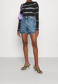 Pantalones cortos de mezclilla de talle alto en azul medio, blusa de rayas negra y blanca de manga larga, sandalias de tacón verdes y un bolso pequeño morado.