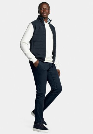 Padded navy vest over a white sweater, paired with dark blue pants and navy shoes. The vest has a high collar and sleek design.