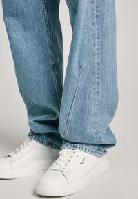 Svijetloplave traperice širokih nogavica s bočnim šavom. Uparene s bijelim tenisicama na vezanje s glatkom završnom obradom i detaljem loga.