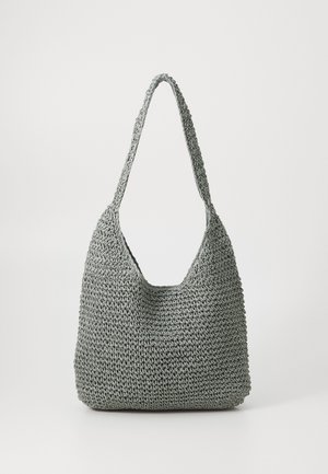 Grå strikket skuldertaske med et tekstureret mønster i åben vævning og en bred rem, stående oprejst på en ensfarvet baggrund.