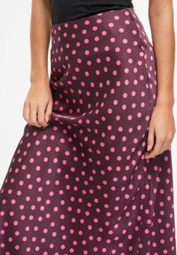 Falda larga de satén con base burdeos oscura y grandes lunares rosas. La tela tiene una textura suave y un ligero brillo.