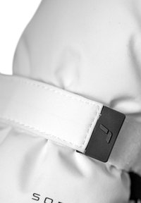 Vit textilvante med en svart plastknäppning, med sömnadsdetaljer och en indragen tyget i sektionen för en tät passform.