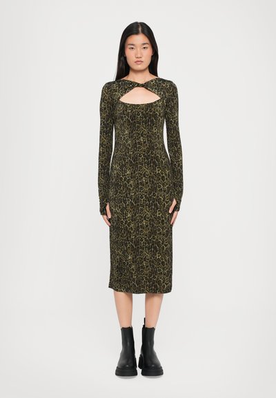 Robe à manches longues en imprimé léopard dans des tons de vert foncé et noir, avec un détail en découpe à l'avant. Associée à des bottines noires.