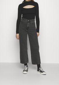 Svart ribbad långärmad topp med en utskärning vid bröstet, tillsammans med högmidjade, vida mörkgrå jeans och svarta sneakers.