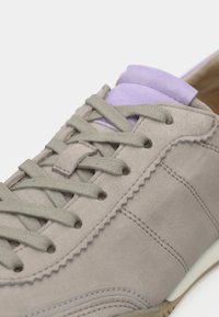 Κοντινή λήψη μπεζ σουέτ αθλητικού παπουτσιού με γκρι κορδόνια και ανοιχτό μωβ μαλακό γλώσσα σε λευκό φόντο.