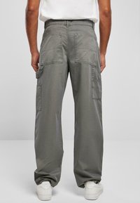 Pantalones cargo grises con un corte holgado, múltiples bolsillos y una textura suave, combinados con zapatillas blancas sobre un fondo neutro.