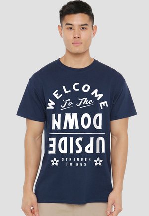 Navy cotton t-shirt featuring large white text reading "WELCOME TO THE UPSIDE DOWN" with "STRANGER THINGS" below. Casual fit.
