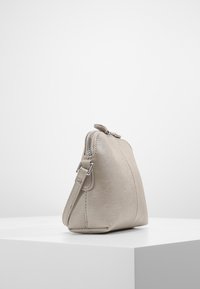 Borsa in pelle beige con forma triangolare, chiusura con zip e tracolla regolabile. Texture liscia e design minimalista.