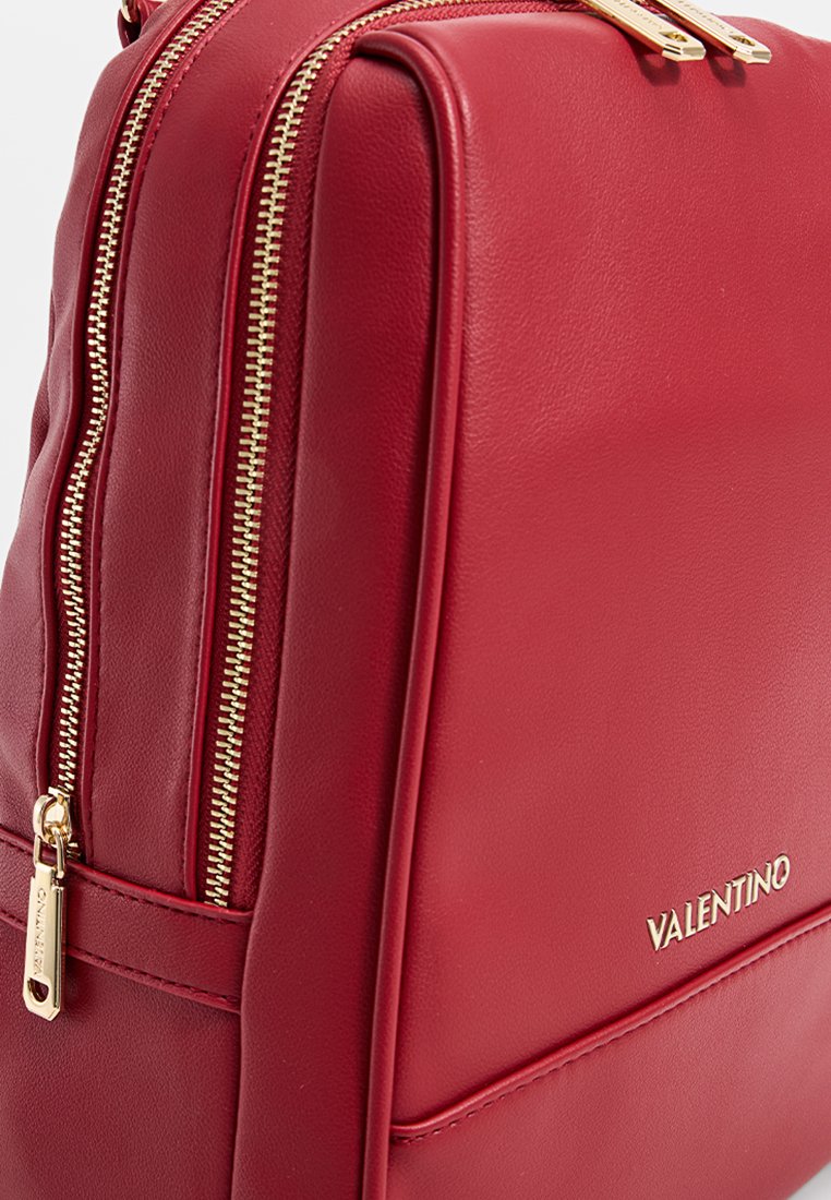 Mochila de cuero rojo con herrajes de cremallera dorados, que presenta una textura suave y el nombre de la marca "VALENTINO" en relieve en el lateral.