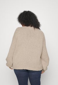 Beige gebreide trui met een losse pasvorm, brede mouwen en een zoom die net onder de taille valt. De textuurrijke garen geeft een gezellige uitstraling.