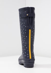 Botte de pluie bleu marine avec des motifs de gouttes de pluie blanches, une bande verticale jaune à l'arrière, et une sangle ajustable près du haut.