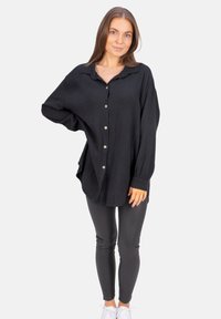 Black button-up shirt in textured waffle fabric with a relaxed fit and long sleeves, paired with shiny black leggings and white sneakers.