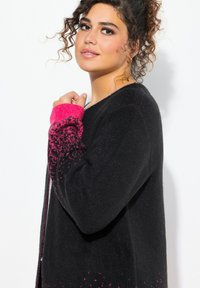 Pull noir avec une finition texturée, doté de poignets dégradés roses et de détails éclaboussés. Conçu avec une coupe décontractée et un col rond.