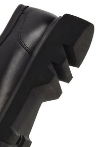 Zwarte leren laars met een dikke, robuuste rubbere zool met diepe groeven en een glad bovenwerk met subtiele stiksels.