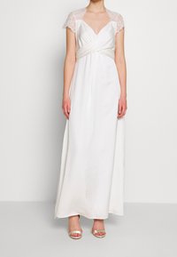 Robe blanche longue jusqu'au sol avec des manches courtes en dentelle et un détail de taille torsadée, présentant une texture satinée lisse et un éclat subtil.