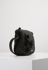 Schwarze synthetische Umhängetasche mit floralen Akzenten, runder Form, verstellbarem Trageriemen und glatter Textur. Verfügt über ein Logo-Tag auf der Vorderseite.