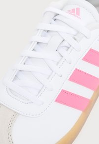 Άσπρο sneaker Adidas με ροζ ρίγες, άσπρα κορδόνια και μπεζ σουέτ κάλυμμα στη μύτη, που δείχνει τις λεπτομέρειες από το πάνω, μπροστινό και πλαϊνό μέρος.