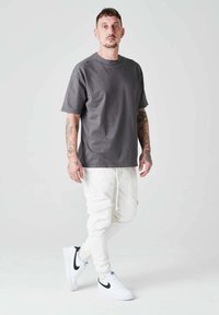 Camiseta de algodón gris con cuello redondo, combinada con pantalones cargo blancos que tienen bolsillos laterales y puños elásticos, completado con zapatillas blancas.