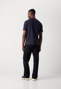 Dunkelblaues Baumwoll-T-Shirt mit Rundhalsausschnitt, kombiniert mit schwarzer, lockerer Hose und beigen Sneakern. Von hinten aufgenommen.