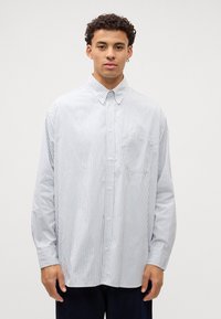 Camisa de botones a rayas en azul claro y blanco, con cuello, mangas largas y un bolsillo en el pecho. Textura de tela suave.
