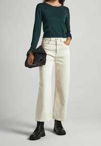 Zielony dziany sweter z długim rękawem, kremowe dżinsy o szerokich nogawkach oraz czarne skórzane botki na sznurowadła. Trzyma czarną teksturowaną torebkę z ozdobnymi ćwiekami.