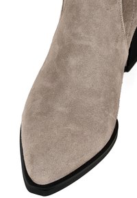 Botine din suede bej, până la gleznă, cu vârf ascuțit, talpă neagră și textură subtle. Fără accesorii sau modele vizibile. Accent pe materialul superior.