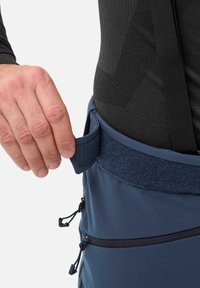 Pantalons d'escalade bleu marine avec une taille ajustable et des poches zippées noires. Boucle en tissu au côté pour saisir, pour le serrage ou l'ajustement.