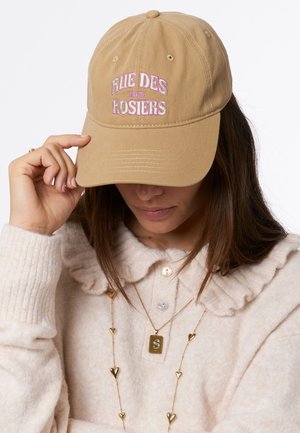 Tan baseball pet met geborduurd "Rue des Rosiers" in roze. Zacht materiaal, gestructureerde vorm en zichtbare stiksels.