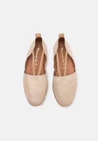 Paire de chaussures plates beige à enfiler avec des brides élastiques et des bouts arrondis, vues de dessus sur un fond uni.