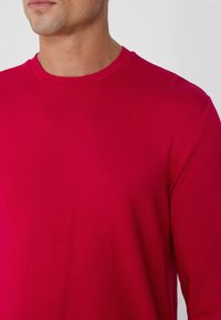 Suéter rojo de manga larga con cuello redondo, fabricado en un tejido suave. Presenta un cuello acanalado y costuras limpias, ofreciendo un ajuste ceñido pero cómodo.