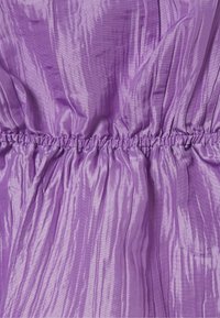 Lila gekräuselter Stoff mit einem gerafften, elastischen Saum, der strukturierte vertikale Falten und einen dezenten Glanz erzeugt.