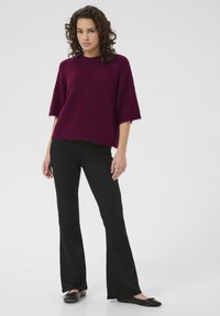 Maglione lavorato a maglia bordeaux con maniche corte, finitura testurizzata e orlo grezzo, abbinato a pantaloni neri svasati e scarpe nere basse.
