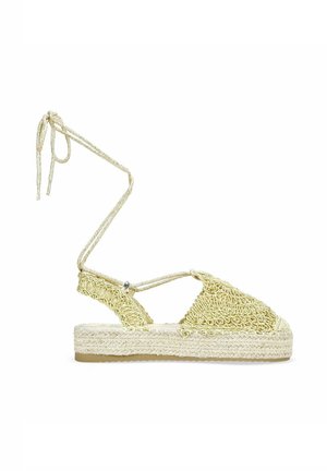 Sandal de esparto amarillo trenzado con lazos en el tobillo, parte superior texturizada, suela de esparto y plataforma plana de yute natural.